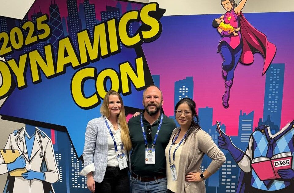 Christina Korff, Stefan Falkenhagen und Linh Schmidt stehen vor einem Banner der DynamicsCon 2025 und blicken in die Kamera