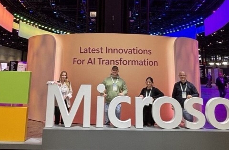 Vier Sven Mahn IT Mitarbeiterinnen und Mitarbeiter stehen hinter einem großen Microsoft-Slogan auf der Microsoft Ignite 2024